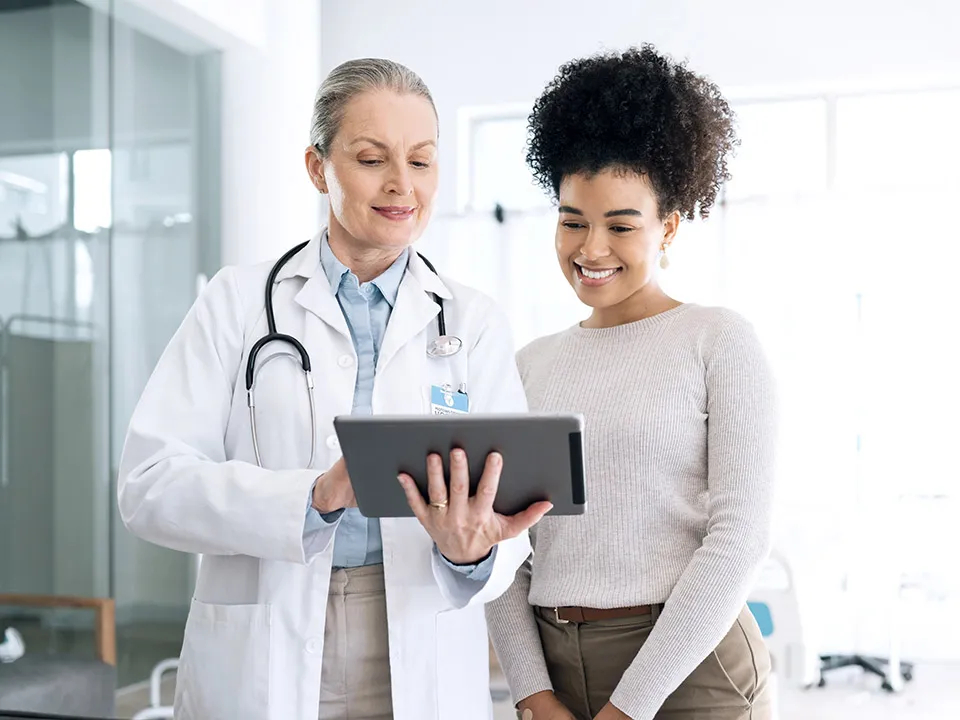 Ärztin und Patientin schauen gemeinsam auf ein Tablet mit Gesundheitsdaten
