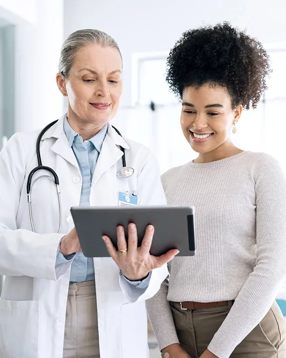 Ärztin und Patientin schauen gemeinsam auf ein Tablet mit Gesundheitsdaten